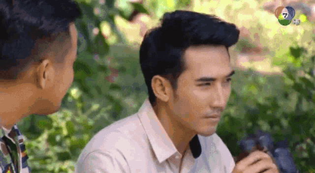 two men are sitting next to each other in the woods and talking .