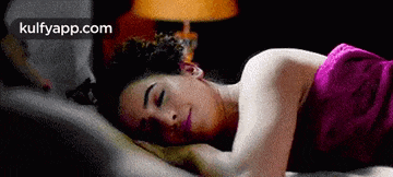 a woman is sleeping on a bed with a pink towel around her waist .