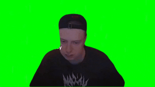 a man wearing a hat and a black shirt is sitting at a desk on a green screen .