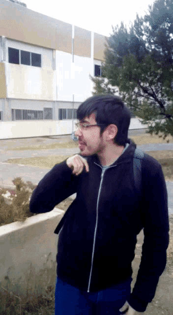 a man wearing glasses and a black jacket is standing in front of a large building