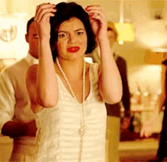 a woman wearing a pearl necklace holds her hair in her hands