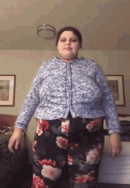 a woman wearing a blue shirt and floral pants is standing in a room