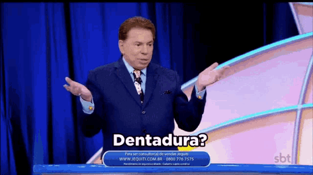 a man in a suit and tie stands on a stage with a sign that says dentadura