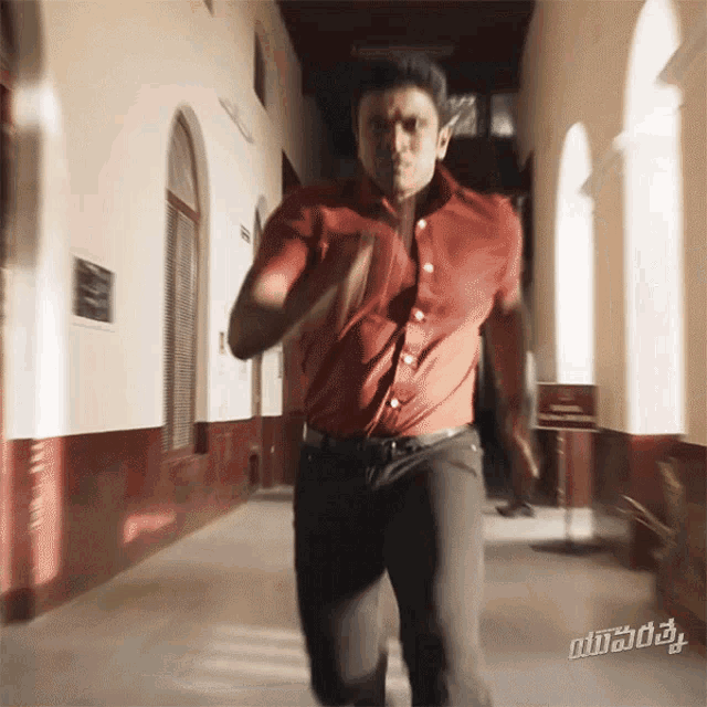 a man in a red shirt and black pants is running down a hallway with a sign that says ' vijay ' on it