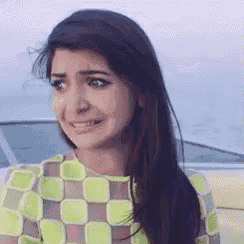a woman with long hair is wearing a green and brown checkered shirt and making a funny face .