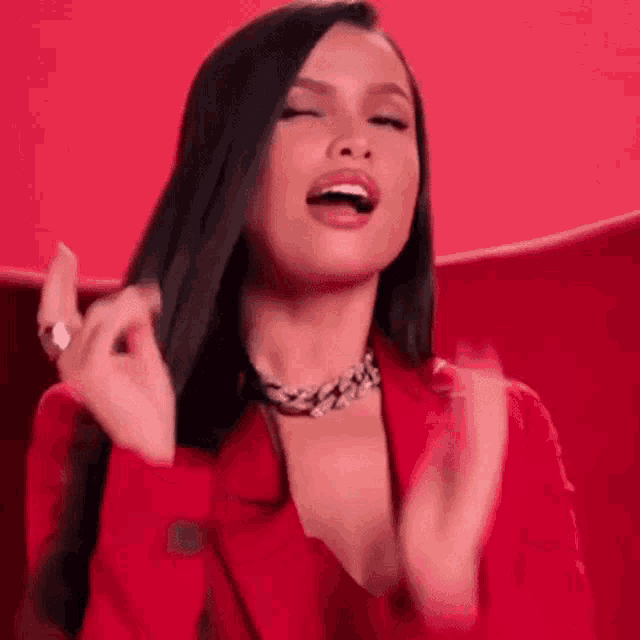 the woman is wearing a red jacket and a necklace and is clapping her hands .