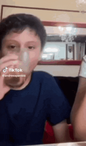 a young boy is drinking a glass of water from a glass .