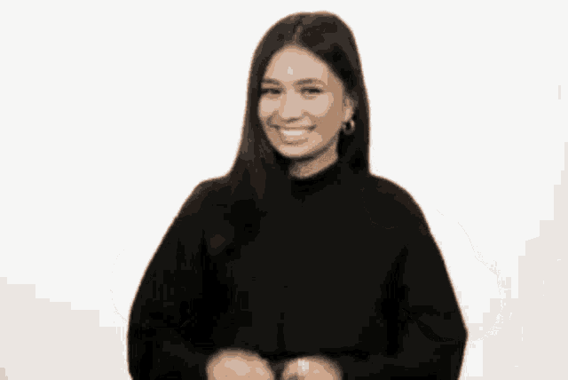 a woman in a black sweater is smiling while holding her hands up