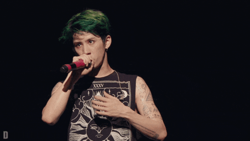 a man with green hair is singing into a microphone with a black shirt that says xxxv