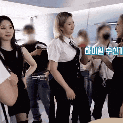 a woman in a white shirt and black pants stands in front of a group of people with korean writing on the bottom right corner