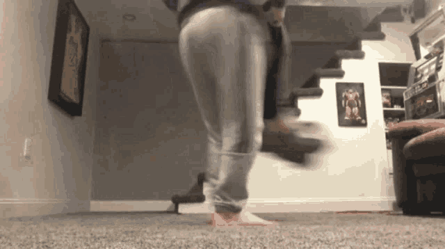 a person is jumping in the air in a living room in front of stairs .
