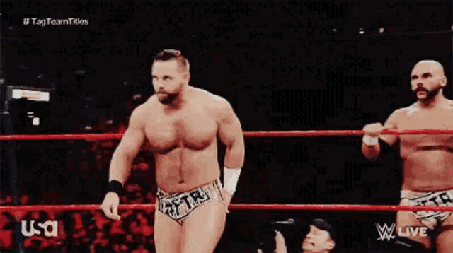 a man is standing in a wrestling ring without a shirt on and holding another man 's hand .