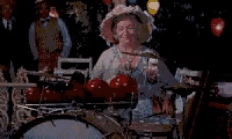an elderly woman in a hat is playing drums