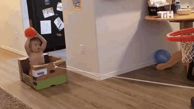 a baby is playing with a ball in a cardboard box with the letters th visible