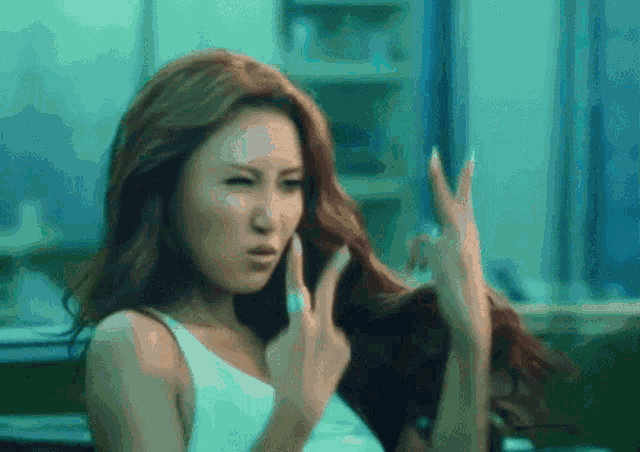 a woman in a white tank top is making a funny face with her hands