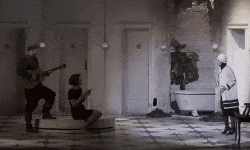 a man is playing a guitar while a woman sits on a stool