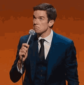 a man in a suit is holding a microphone and making a face .