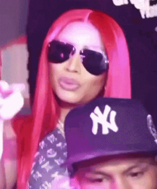 a woman with pink hair wearing sunglasses and a ny hat .