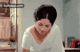 a woman in a white saree is standing in a room with her head down .