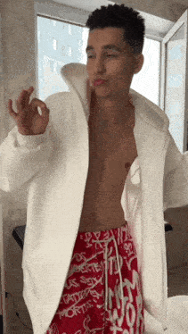 a shirtless man wearing a white jacket and red shorts with graffiti on them
