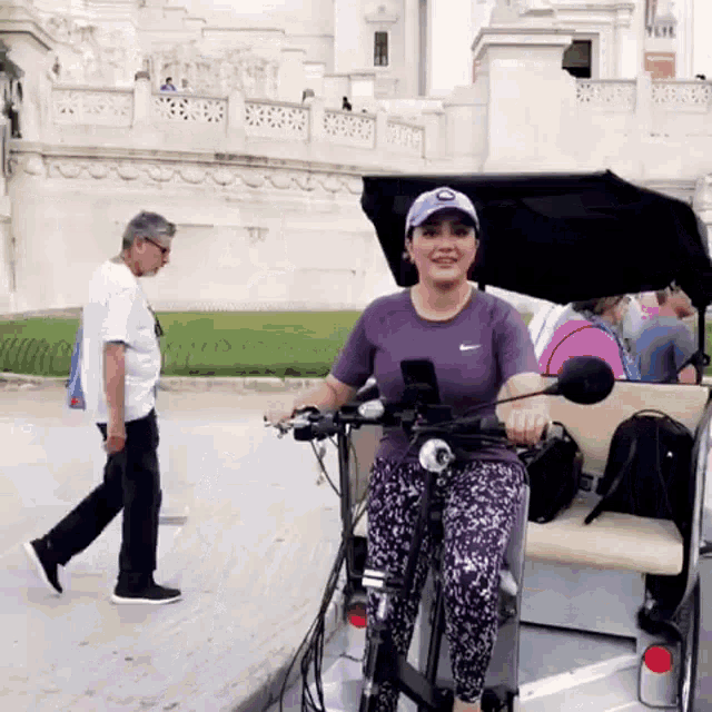 a woman in a purple shirt is riding a bike