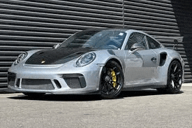 a silver porsche 911 gt3 rs is parked in front of a striped wall .