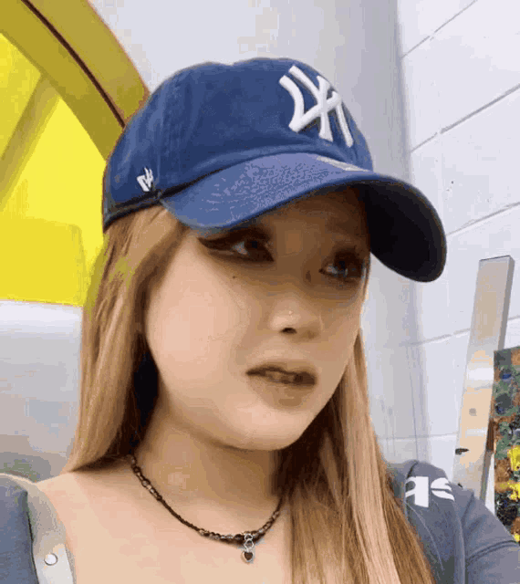 a woman wearing a blue ny yankees hat looks at the camera