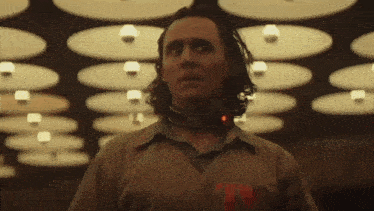 a man with long hair and a collar around his neck is standing in front of a ceiling .