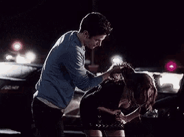 a man and woman are standing next to each other in a parking lot at night