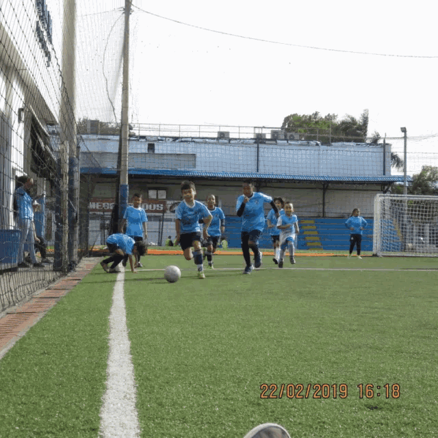 a group of children are playing soccer on a field with a photo taken on 22/02/2019