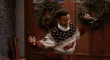 a man wearing a christmas sweater and gloves is dancing in a room .