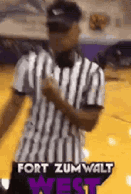 a referee in a striped shirt is standing on a basketball court holding a microphone .
