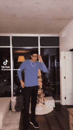 a man in a blue sweater and black pants is standing in front of a christmas tree in a living room