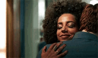 a woman with curly hair is hugging a man .