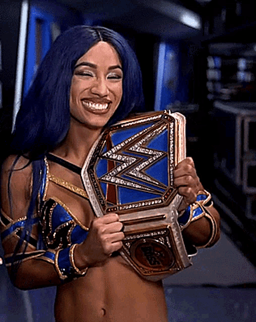a woman with blue hair is holding a wrestling championship belt and smiling