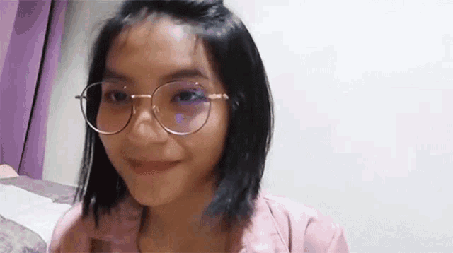 a girl wearing glasses and a pink jacket is smiling .