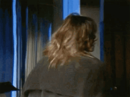 a woman in a trench coat is standing in front of a window with blue curtains .