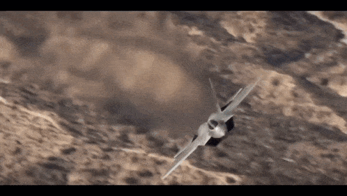a fighter jet is flying in the air over a desert landscape .