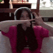 a woman wearing headphones and a pink shirt is making a peace sign .