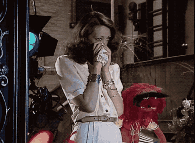 a woman covering her mouth with her hand while standing next to a red muppet