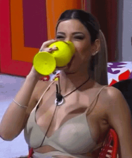 a woman is drinking from a yellow cup while wearing a bra .