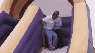a couple of people are standing on top of a purple and yellow bouncy house .