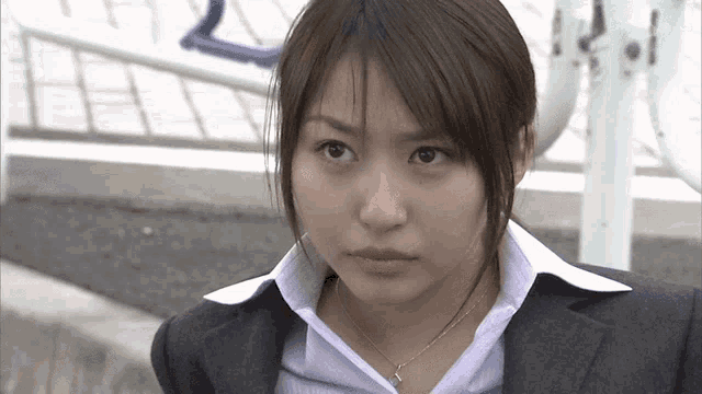 a woman wearing a suit and a necklace is looking at the camera