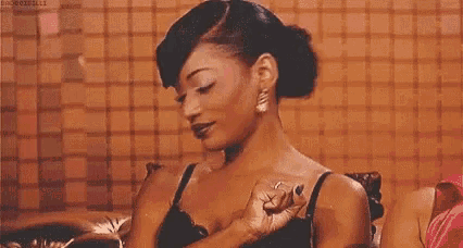 a woman in a black bra and earrings is sitting on a couch holding her chest .