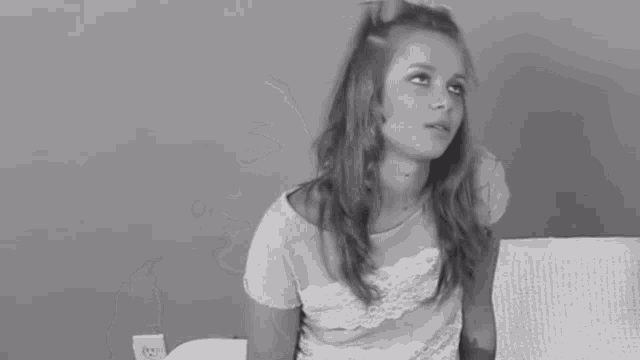 a black and white photo of a young girl sitting on a couch looking to the side .