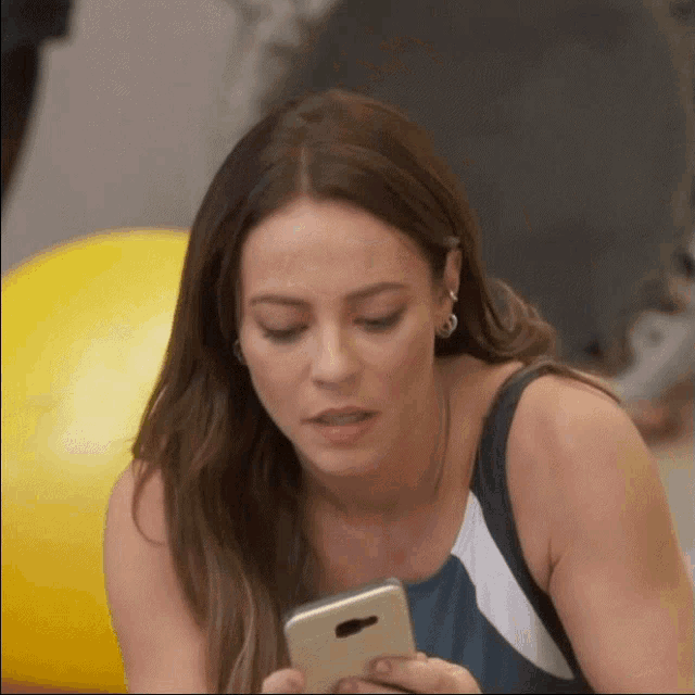 a woman in a blue tank top is looking at her phone