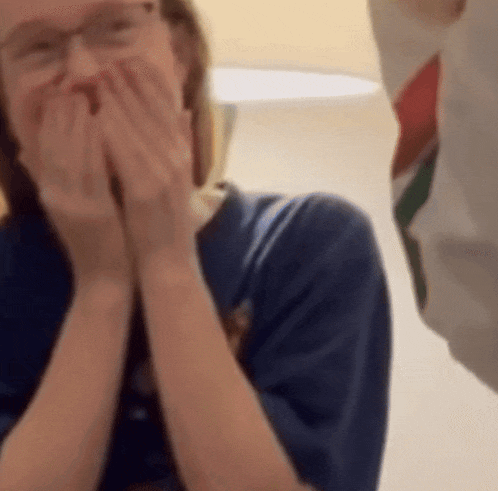 a woman covering her mouth with her hands while wearing glasses