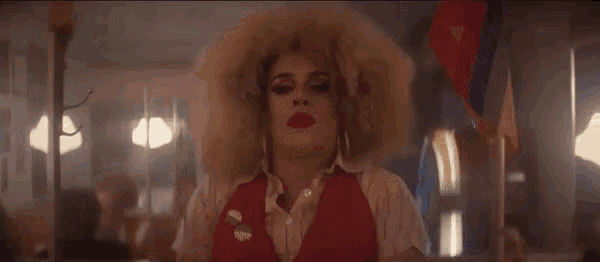 a drag queen is standing in a diner wearing a red vest and red lipstick .