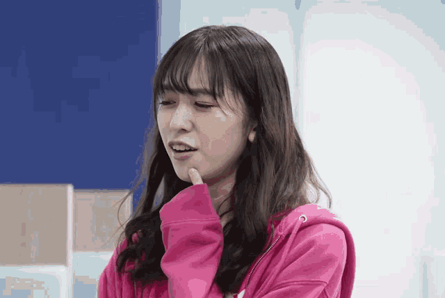 a woman wearing a pink hoodie holds her hand to her chin