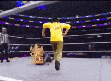 a man in a yellow shirt is running in a wrestling ring with the letters rcb on it